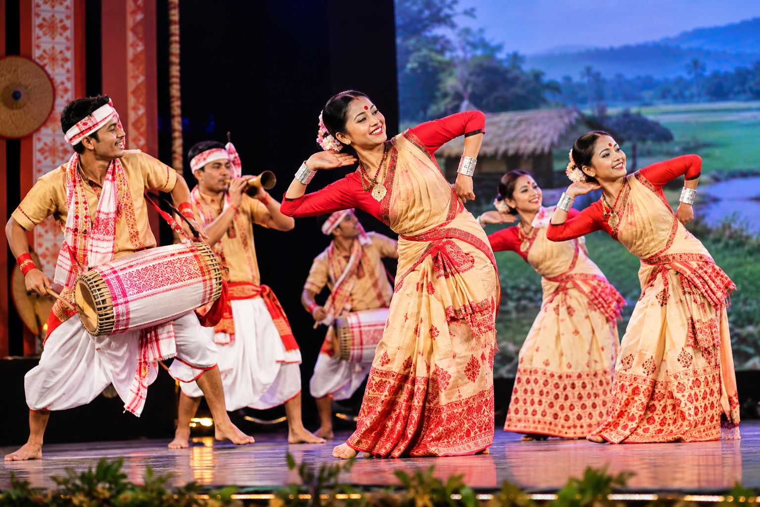 Bihu dance performance on stage with Assamese dancers in traditional costume and a dhol player leading the rhythm