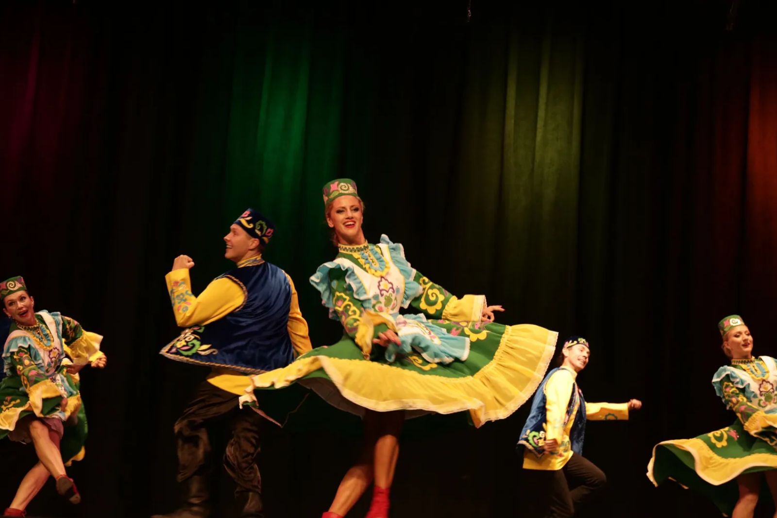 Russian folk dance ensemble in traditional sarafan and kokoshnik costumes performing on a lit stage